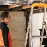 Un homme en veste orange et noire observe le plafond délabré d'un bâtiment, signe d'une future rénovation énergétique des bâtiments publics.