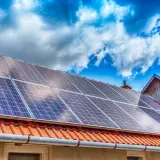 Panneaux solaires sur un toit de tuiles rouges sous un ciel bleu et nuageux. Une installation qui peut influencer le coût de l'assurance photovoltaïque.