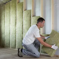 Pose d'isolant minéral pour respecter la norme isolation thermique rénovation. Un ouvrier installe des panneaux dans une structure en bois.