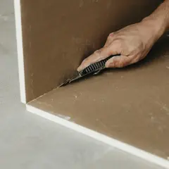 Main d'un artisan coupant une plaque de Fermacell ou de Placo avec un cutter. Travaux de rénovation en cours.
