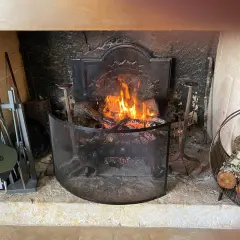 Un feu de bois crépite dans une cheminée. Des outils de cheminée et du bois sont à proximité, prêts à fabriquer un récupérateur de chaleur pour poêle à bois.