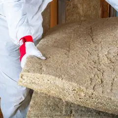 Un ouvrier en combinaison blanche manipule un panneau de laine de bois soufflée, prêt à isoler une maison.