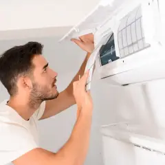 Un homme nettoie la climatisation de sa maison, retirant le filtre pour un entretien.