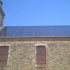 Panneaux solaires installés sur le toit d'un bâtiment en pierre, possiblement dans une zone classée, sous un ciel bleu clair.