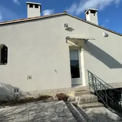 Maison Phénix 1970, blanche, avec cheminées, sous un ciel bleu. Escalier en pierre menant à la porte.