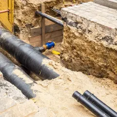 Gros tuyaux noirs enfouis dans le sable, prêts pour le chauffage urbain. Des travaux de voirie en cours.