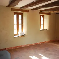 Murs en chaux chanvre pour une isolation naturelle et saine. Plancher de terre cuite et poutres apparentes dans une pièce lumineuse.