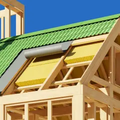Structure en bois d'une maison avec toiture verte et isolation par l'extérieur jaune visible.