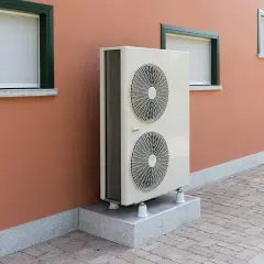 Unité extérieure d'une pompe à chaleur géothermique, installée sur un socle devant un mur ocre. Le prix de ce système est un investissement pour le confort.