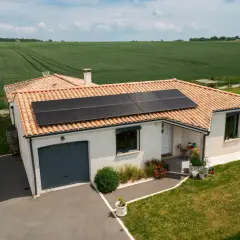 Maison avec toiture photovoltaïque, entourée de verdure et de champs.