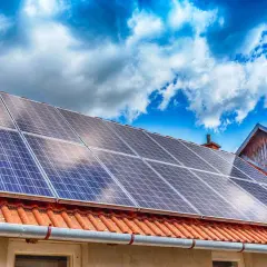 Panneaux solaires sur un toit de tuiles rouges sous un ciel bleu et nuageux. Une installation qui peut influencer le coût de l'assurance photovoltaïque.