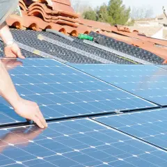 Installation de panneaux solaires sur un toit. Une main ajuste un panneau, préparant la revente du surplus photovoltaïque sans RGE.