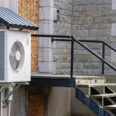 Unité extérieure de climatisation sous un auvent, près d'un escalier en métal et en bois. Idéal pour savoir où placer sonde température extérieure.