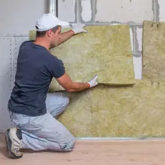 Un ouvrier installe un panneau d'isolation minérale. Il pose la laine de roche pour une meilleure isolation thermique et phonique.