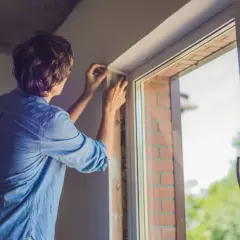 Un homme en chemise bleue ajuste le cadre d'une nouvelle installation fenêtre.