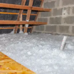 Gros plan sur l'isolation des combles perdus, une épaisse couche de ouate de cellulose recouvre le sol. Une règle mesure l'épaisseur.