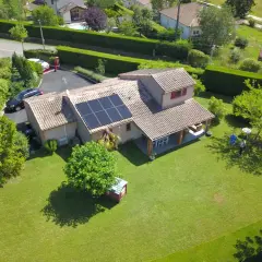 Maison avec panneaux photovoltaïques sur le toit, jardin verdoyant, piscine et deux personnes discutant.