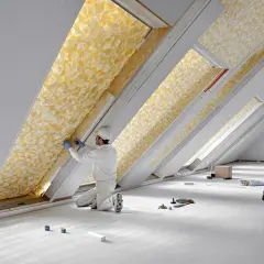 Un ouvrier installe un isolant jaune texturé dans un grenier, étape clé de la transition éco-énergie pour une meilleure isolation.