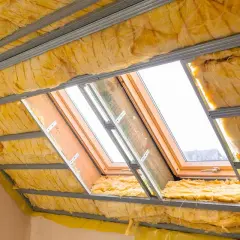 Isolation des combles aménageables avec laine de verre jaune sous une structure métallique. Des fenêtres de toit laissent passer la lumière.