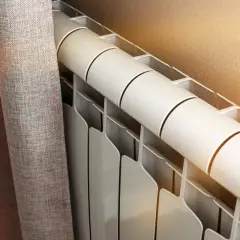 Radiateur blanc près d'un rideau gris. Le fluide caloporteur circule pour chauffer la pièce.