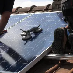 Un installateur panneau solaire agréé manipule un panneau sur un toit. Des ventouses sont prêtes à aider.