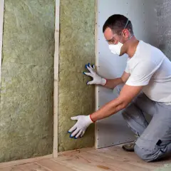 Un ouvrier installe une isolation minérale dans un mur, respectant la norme isolation phonique RT 2012.