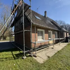 Échafaudage autour d'une maison en briques rouges, signe d'une rénovation maison de ville en cours. Le soleil brille sur le chantier.