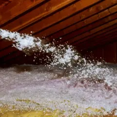Un tuyau souffle de l'isolant dans un grenier. Attention au sel de bore, un danger potentiel pour la santé.