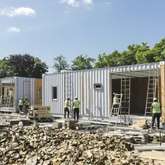 Chantiers de construction d'une maison container. Des ouvriers en gilets de sécurité travaillent sur des modules préfabriqués.