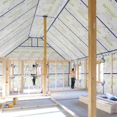 Construction d'une maison avec membrane d'étanchéité à l'air obligatoire. Des ouvriers installent la membrane sur les murs et le toit.