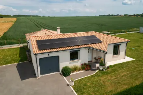 Maison avec toiture photovoltaïque, entourée de verdure et de champs.