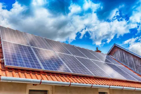 Panneaux solaires sur un toit de tuiles rouges sous un ciel bleu et nuageux. Une installation qui peut influencer le coût de l'assurance photovoltaïque.