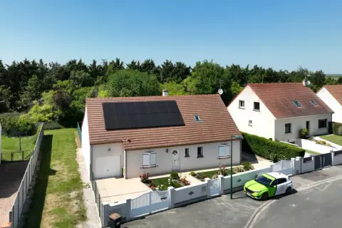 Maison avec panneaux photovoltaïques en vente, un véhicule vert et blanc garé devant.