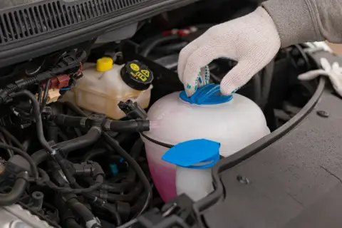 Main d'une personne portant un gant blanc ferme le bouchon d'un vase d'expansion rempli d'eau et de liquide de refroidissement rose.