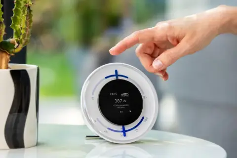 Un doigt effleure un écran affichant "387 W CONSOMMATION RÉSEAU", utile pour comment suivre sa production photovoltaïque EDF.