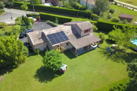 Maison avec panneaux photovoltaïques sur le toit, jardin verdoyant, piscine et deux personnes discutant.