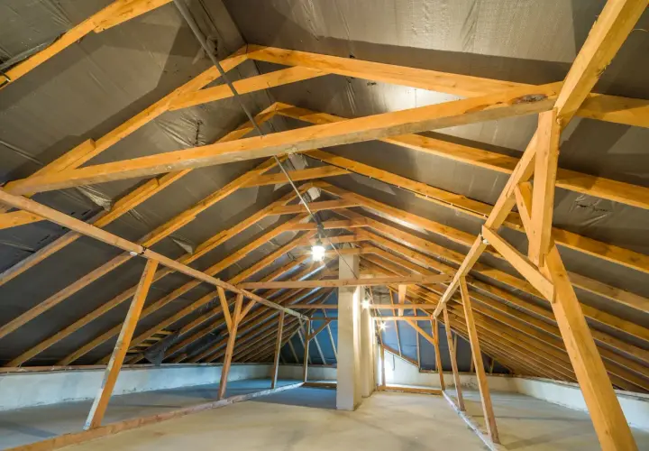 Charpente en bois d'un grenier en cours d'aménagement, avec une bâche noire recouvrant la structure de la r toiture.