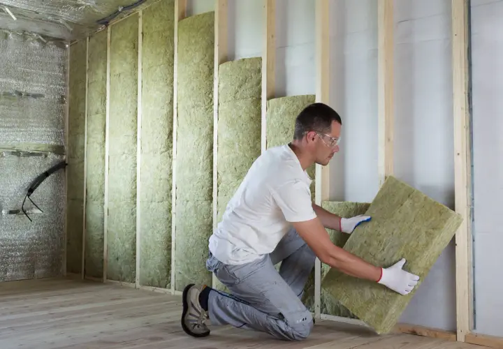 Pose d'isolant minéral pour respecter la norme isolation thermique rénovation. Un ouvrier installe des panneaux dans une structure en bois.
