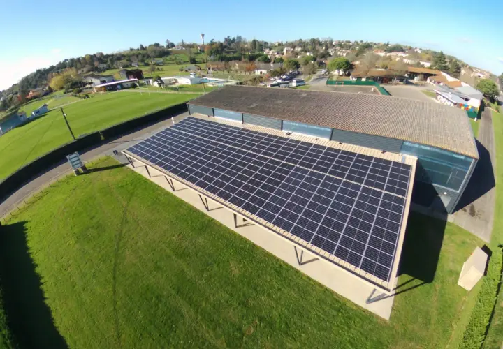 Panneaux solaires sur un bâtiment, assurant une rentabilité 100 kw photovoltaïque. Le paysage environnant est verdoyant.