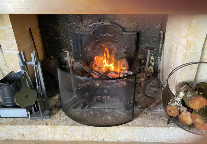 Un feu de bois crépite dans une cheminée. Des outils de cheminée et du bois sont à proximité, prêts à fabriquer un récupérateur de chaleur pour poêle à bois.