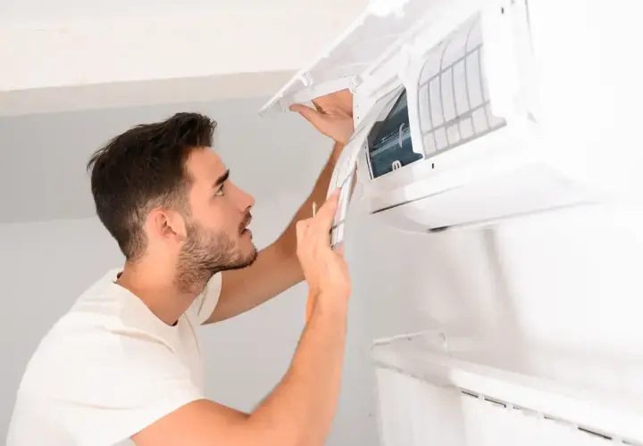 Un homme nettoie la climatisation de sa maison, retirant le filtre pour un entretien.