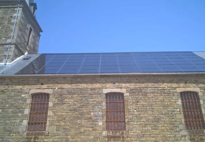 Panneaux solaires installés sur le toit d'un bâtiment en pierre, possiblement dans une zone classée, sous un ciel bleu clair.