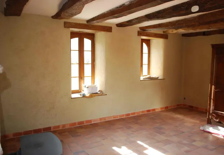 Murs en chaux chanvre pour une isolation naturelle et saine. Plancher de terre cuite et poutres apparentes dans une pièce lumineuse.