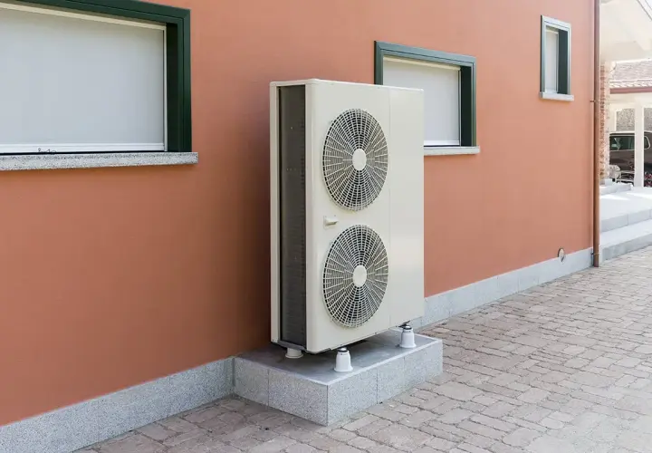 Unité extérieure d'une pompe à chaleur géothermique, installée sur un socle devant un mur ocre. Le prix de ce système est un investissement pour le confort.