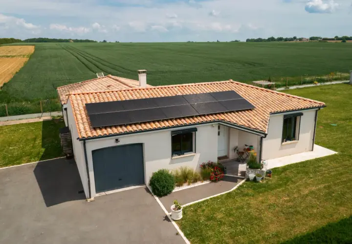 Maison avec toiture photovoltaïque, entourée de verdure et de champs.