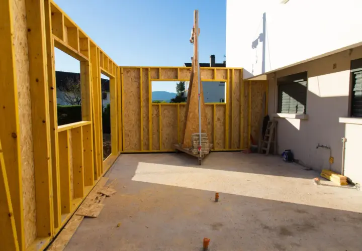 Chantier d'une extension bois, murs en ossature jaune et panneaux OSB, avec vue sur le paysage.