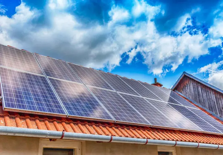 Panneaux solaires sur un toit de tuiles rouges sous un ciel bleu et nuageux. Une installation qui peut influencer le coût de l'assurance photovoltaïque.