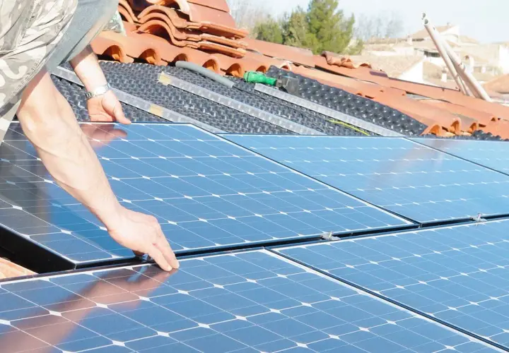 Installation de panneaux solaires sur un toit. Une main ajuste un panneau, préparant la revente du surplus photovoltaïque sans RGE.