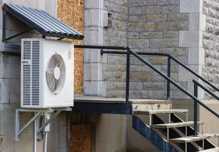Unité extérieure de climatisation sous un auvent, près d'un escalier en métal et en bois. Idéal pour savoir où placer sonde température extérieure.