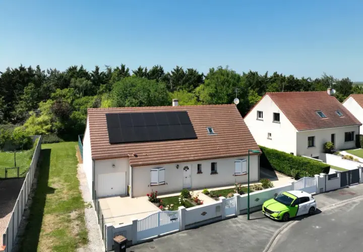 Maison avec panneaux photovoltaïques en vente, un véhicule vert et blanc garé devant.